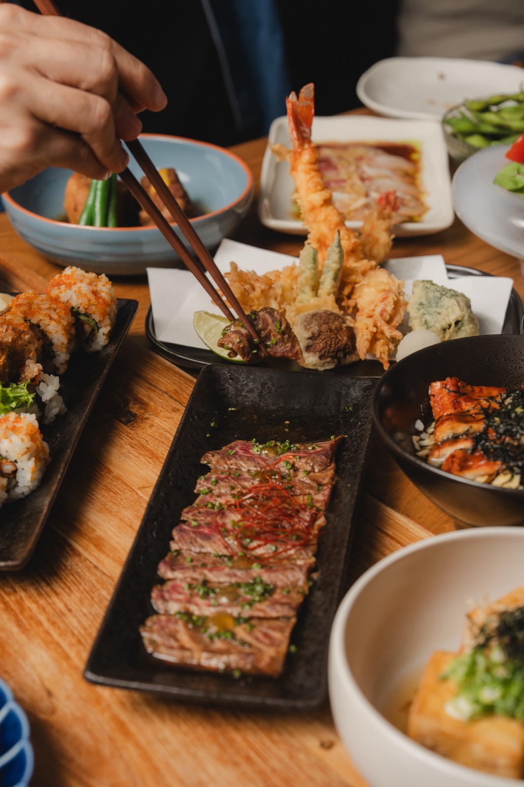 Chopsticks reaching across a table of tempura, sushi and wagyu